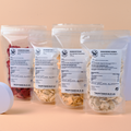 Frucht-Bundle: vier transparente Doypacks mit gefriergetrockneten Früchten – Erdbeeren, Ananas, Mango und Banane vor apricotfarbenem Hintergrund