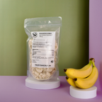 Gefriergetrocknete Bananenscheiben im transparenten Doypack neben einem Bündel ganzer Bananen