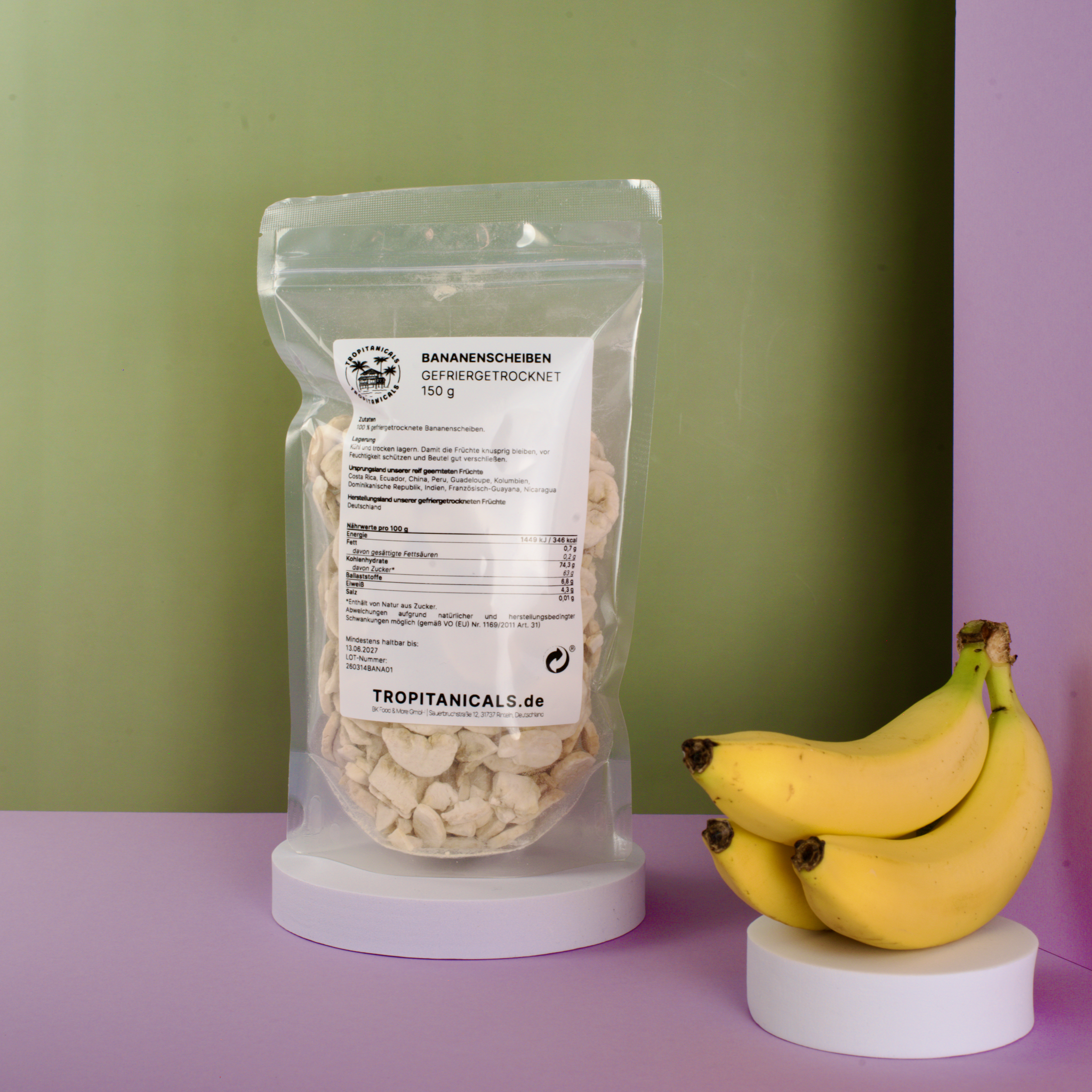 Gefriergetrocknete Bananenscheiben im transparenten Doypack neben einem Bündel ganzer Bananen