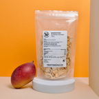 Gefriergetrocknete Mango im Doypack auf einem weißen Podest mit einer frischen Mango