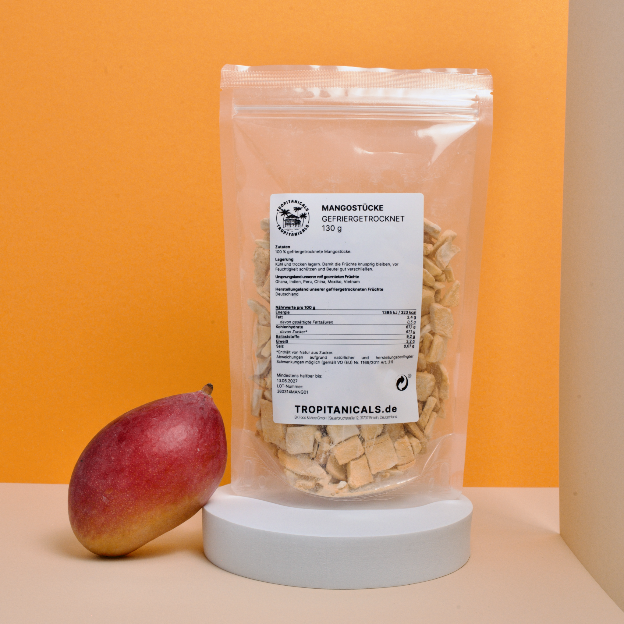 Gefriergetrocknete Mango im Doypack auf einem weißen Podest mit einer frischen Mango